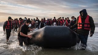 Migranten ziehen ein Schlauchboot aus dem Wasser am Strand von Gravelines. 