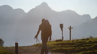 Wanderer mit Rucksack und Trekkingstöcken im Gegenlicht vor Bergkulisse unterwegs zur Gotzenalm, Schönau am Königssee, Berchtesgadener Land