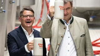 Markus Söder (CSU), Ministerpräsident von Bayern, und Boris Rhein (CDU), Ministerpräsident von Hessen, halten bei der Besichtigung der Brauerei Glaabsbräu in Seligenstadt Bierkrüge in den Händen.