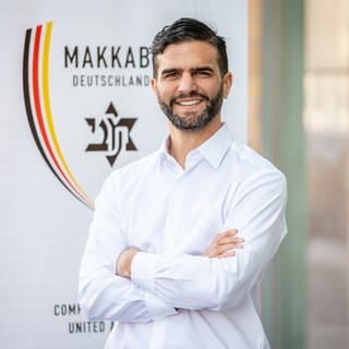 Alon Meyer, Präsident von Makkabi Deutschland, steht vor dem Logo.
