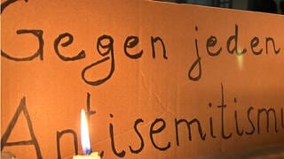 Eine brennende Kerze steht vor einem Schild mit der Aufschrift "Gegen jeden Antisemitismus"