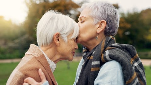 Seniorin küsst eine andere Frau auf die Stirn