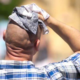 Ein Mann wischt sich mit einem Stofftuch über den Kopf.