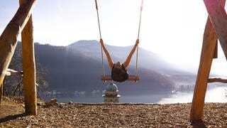 Frau auf einer Schaukel mit Bergblick und Sonnenlicht über dem Luganer See in Morcote, Tessin in der Schweiz. Symbolfoto