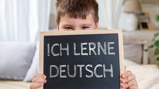 Kind hält eine Tafel mit der Aufschrift: Ich lerne Deutsch. Sprachunterricht und Migration