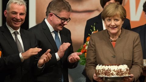 Bundeskanzlerin Angela Merkel mit Parteikollegen. Sie hält eine Schwarzwälder Kirschtorte in Händen.