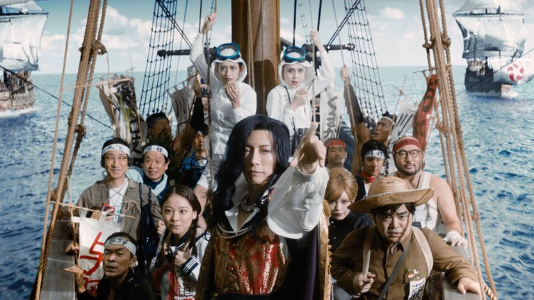 Menschen schauen auf einem Schiff in die Kamera, Filmszene aus dem japanischen Kinofilm "Fly Me To The Saitama -FROM BIWA LAKE WITH LOVE" von Hideki TAKEUCHI