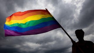 Eine Frau trägt bei der Gedenkfeier für die sogenannten Rosa-Winkel-Häftlinge des Konzentrationslagers Buchenwald die Regenbogenfahne am Gedenkstein.