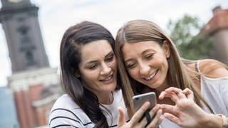 ILLUSTRATION - Zwei junge Frauen schauen sich am 10.08.2017 in einem Park in Hamburg ihre Fotos auf ihrem Smartphone an