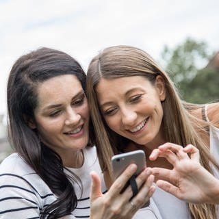 ILLUSTRATION - Zwei junge Frauen schauen sich am 10.08.2017 in einem Park in Hamburg ihre Fotos auf ihrem Smartphone an