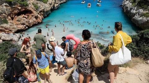 Menschen stehen Schlange am Strand Calo des Moro in Mallorca, einem der überfüllten Strände Mallorcas.