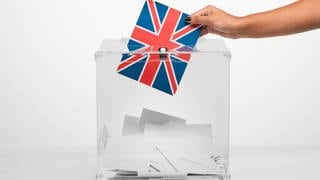 Person, die eine Karte mit der Flagge des Vereinigten Königreichs in die Wahlurne wirft