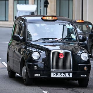 Ein schwarzes Taxi (Black Cab) fährt in der Innenstadt auf der Straße.London