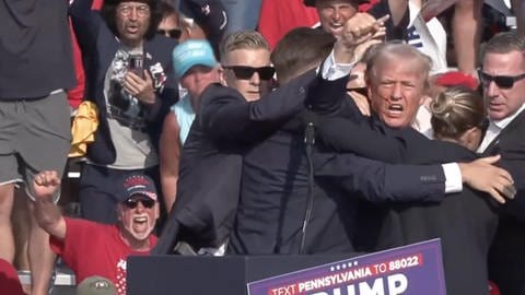 Aufnahme des Trump-Attentats: Donald Trump mit blutendem Ohr wird von seiner Security von der Bühne gezogen