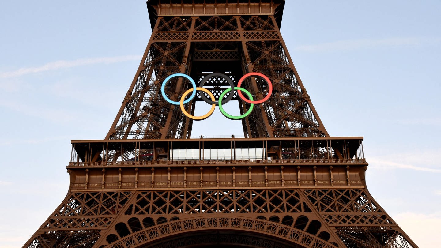 Touristen machen Fotos von den beleuchteten olympischen Ringen auf dem Eiffelturm in Paris