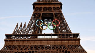 Touristen machen Fotos von den beleuchteten olympischen Ringen auf dem Eiffelturm in Paris