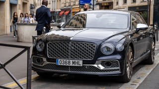 Ein Bentley parkt in der Innenstadt von Paris, Frankreich, umgeben von Fußgängern und stilvoller Architektur. 