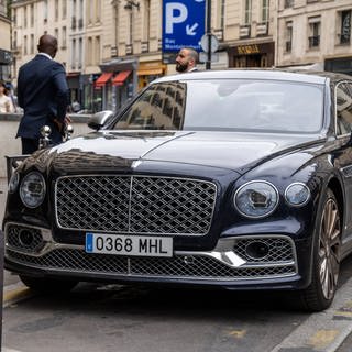 Ein Bentley parkt in der Innenstadt von Paris, Frankreich, umgeben von Fußgängern und stilvoller Architektur. 