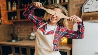 Eine Hausfrau versteckt ihre Augen mit zwei Kochlöffeln.