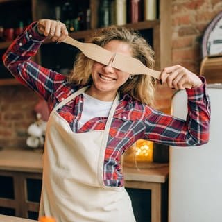 Eine Hausfrau versteckt ihre Augen mit zwei Kochlöffeln.