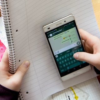 Eine Schülerin sitzt mit ihrem Handy und ihren Schulsachen an einem Schreibtisch.