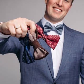 Smiling man insmart suit keeping bow ties in hand Selective focus of smiling man keeping bow ties in hand on isolated background. Symbolfoto