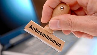 Eine hand hält einen Holzstempel mit dem Aufdruck "Antisemitismus"