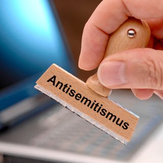 Eine hand hält einen Holzstempel mit dem Aufdruck "Antisemitismus"