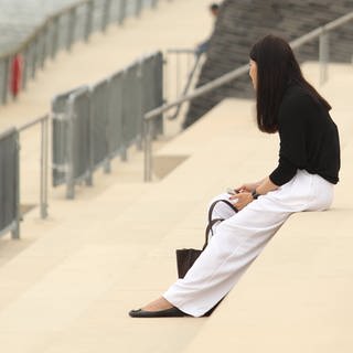 Eine Frau sitzt ganz allein auf einer Treppe am Rheinufer. Symbolbild