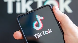 Hand hält Handy mit TikTok-Logo auf dem Display