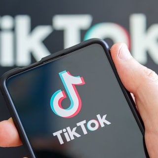 Hand hält Handy mit TikTok-Logo auf dem Display