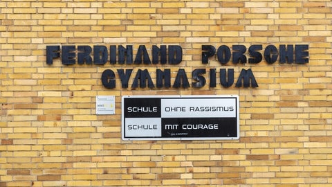 Schriftzug des Ferdinand Posche Gymnasiums auf einer Backsteinwand. Darunter ein Schild mit den Worten: Schule ohne Rassismus, Schule mit Courage.