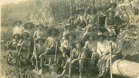 Schwarz-Weiß-Foto Gruppenbild deutsche Koloisten mit Schubkarren und Schaufeln