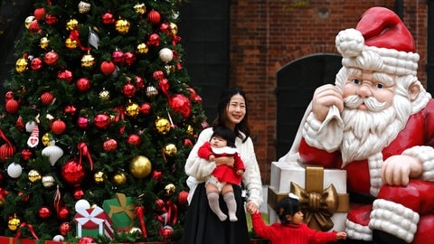 Mutter mit Baby vor geschmücktem Weihnachtsbaum in Japan