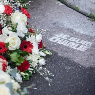 Blumengesteck auf der Straße neben "Je suis Charlie"