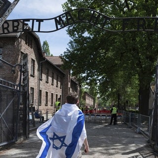 Jüdischer Jugendlicher mit der Israel-Flagge vor dem Eingang zum Nazi-Konzentrationslager Auschwitz mit dem Schriftzug "Arbeit macht frei"