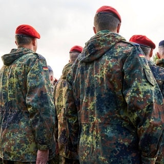 Soldaten der Bundeswehr stehen in Reih und Glied, gekleidet in Flecktarnuniformen und tragen rote sowie blaue Baretts.