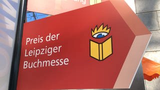 Ein rotes Schild in Pfeilform mit der Aufschrift "Preis der Leipziger Buchmesse" und dem gelben Buchlogo der Buchmesse