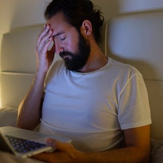 Mann mit Laptop hat zu Hause im Bett Kopfschmerzen