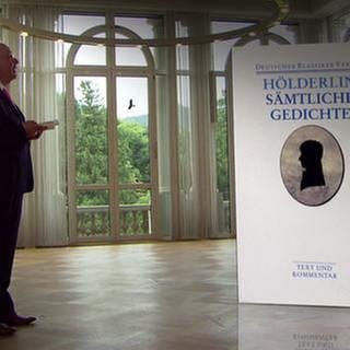 Denis Scheck steht neben dem Buch "Sämtliche Gedichte" von Friedrich Hölderlin