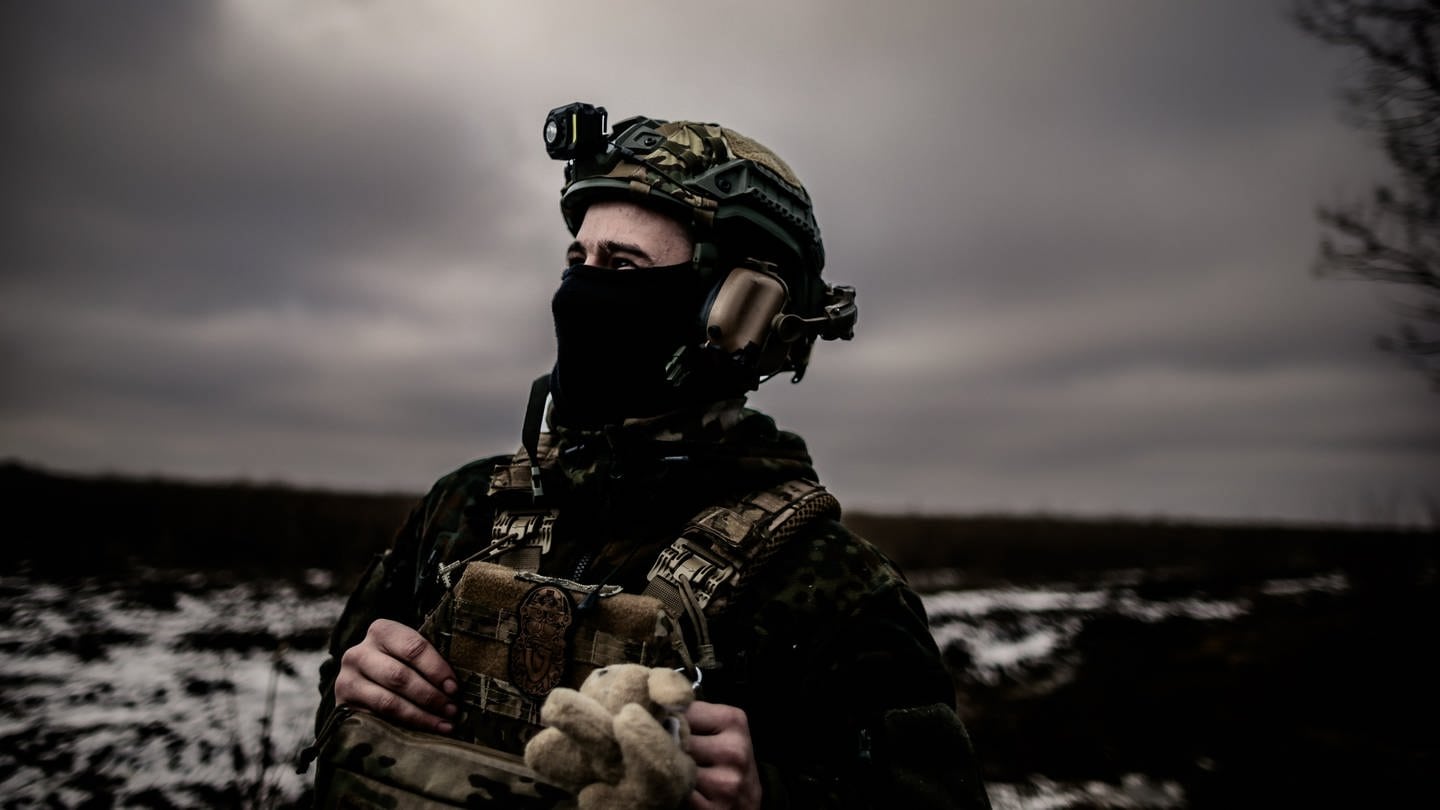 Ein Soldat mit Stofftier an der Uniform blickt ernst in den Himmel