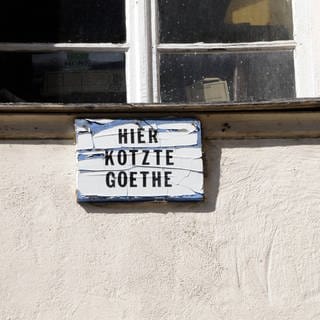 Ein Pappschild mit der Aufschrift "Hier kotzte Goethe" unter einem Fenster an einer Hauswand