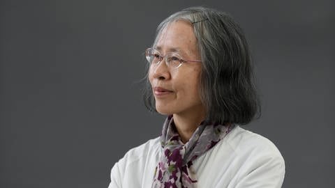 Porträt der Schriftstellerin Can Xue im Rahmen des Edinburgh International Book Festival 2019. Die Chinesin posiert in einer weißen Bluse und mit einem grauen Schal vor einem grauen Hintergrund.