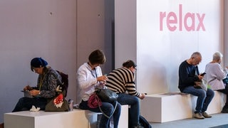 Besucher der Frankfurter Buchmesse sitzen auf Bänken in einer Relaxzone