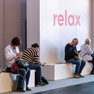 Besucher der Frankfurter Buchmesse sitzen auf Bänken in einer Relaxzone