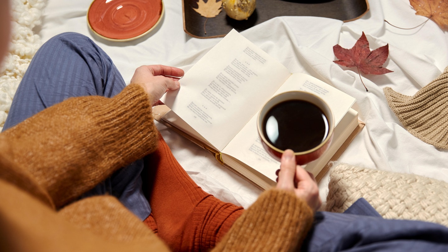 Person mit Tasse und Buch in der Hand, herbstlich geschmückt