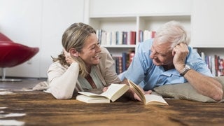 Glückliches Paar liegt auf dem Boden und liest gemeinsam Bücher.