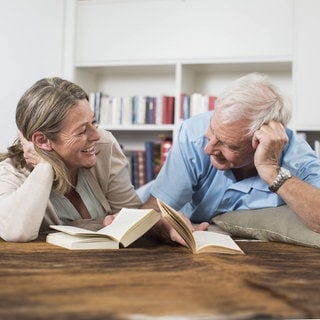 Glückliches Paar liegt auf dem Boden und liest gemeinsam Bücher.