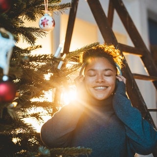 junge Frau mit Kopfhören vor Weihnachtsbaum