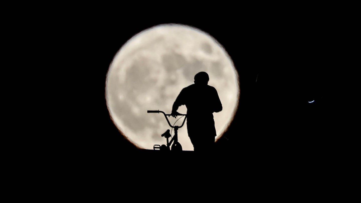 Silhouette eines Mannes mit Fahrrad vor dem tiefstehenden Mond